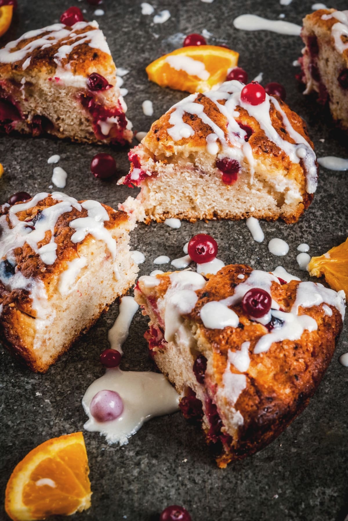 Slices of orange cranberry cake drizzled with icing, garnished with cranberries and orange wedges