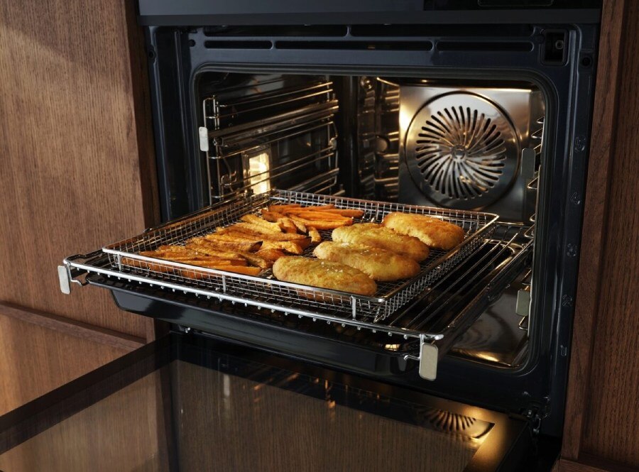 Inside an Electrolux built-in convection oven roasting sweet potato fries and chicken evenly on a wire rack