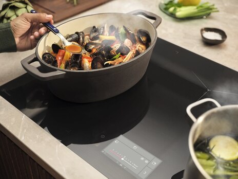 Cook tasting broth from a steaming seafood pot on an induction cooktop