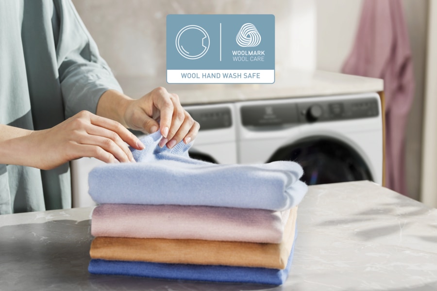 Folding wool clothes next to Woolmark-certified washer