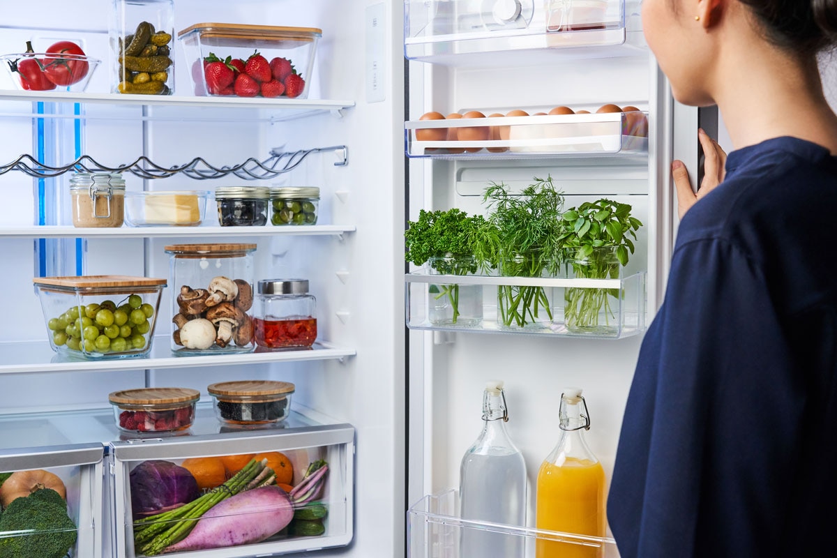Woman open a refrigerator stocked with fresh food and produce.