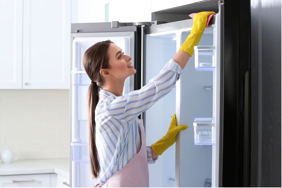 Woman in yellow gloves cleaning an open refrigerator.