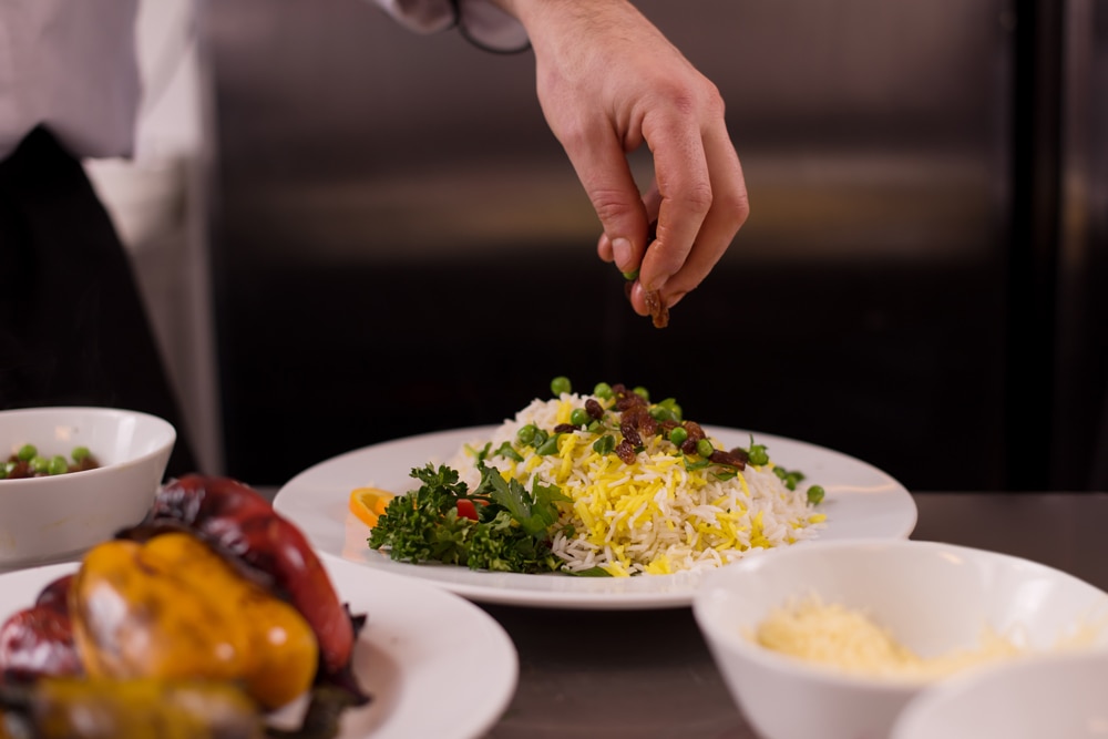 Hand sprinkling garnish over biryani plate