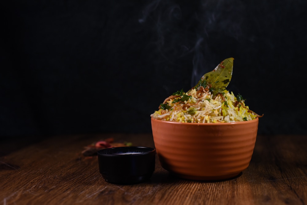 Steaming bowl of veg biryani with side dish 
